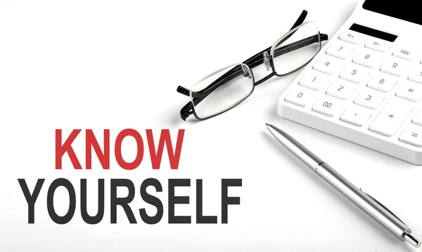 KNOW YOURSELF Concept. Calculator,pen and glasses on a white background