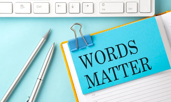 WORDS MATTER text on sticker on blue background with pen and keyboard