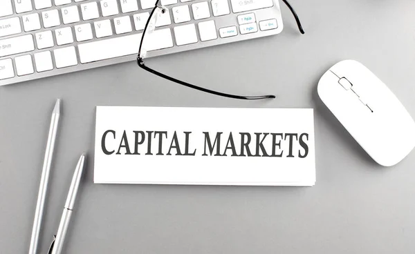 CAPITAL MARKETS text on a paper with keyboard on grey background