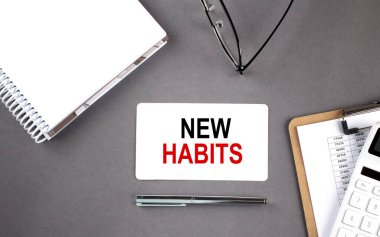 Not defteri ve pano ile karta yazılmış NEW HABITS metni, gri arkaplan