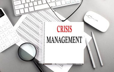 CRISIS MANAGEMENT Gri arkaplan üzerinde klavye ve hesap makinesi ile not defteri üzerinde metin
