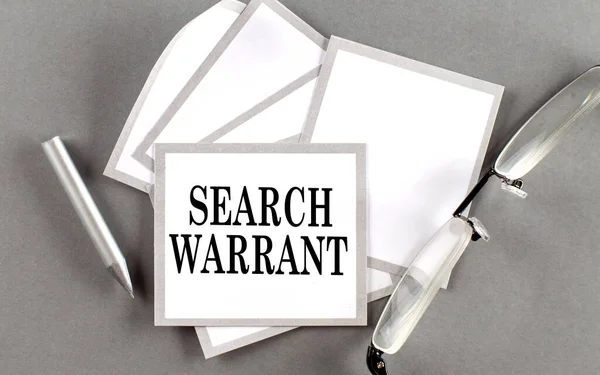 SEARCH WARRANT text written on sticky with pencil and glasses