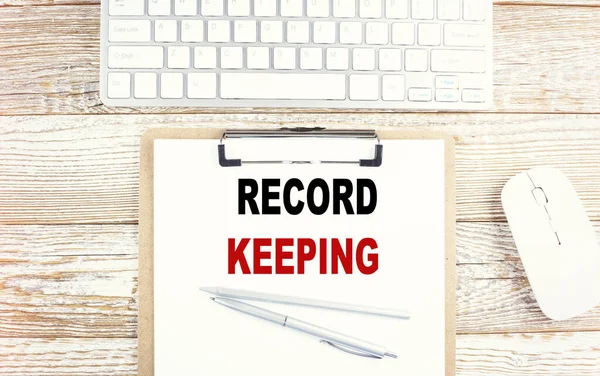 RECORD KEEPING text on clipboard with keyboard on wooden background