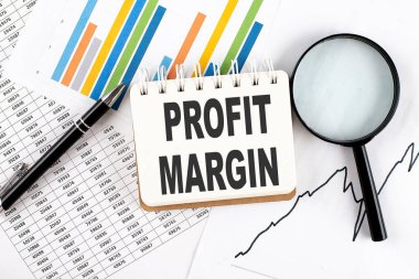 Grafik arkaplanındaki bir defter üzerinde kalem ve büyüteçle PROFIT MARGIN metni