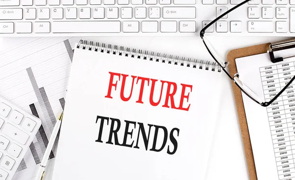 Text FUTURE TRENDS on Office desk table with keyboard, notepad and analysis chart on a white background.
