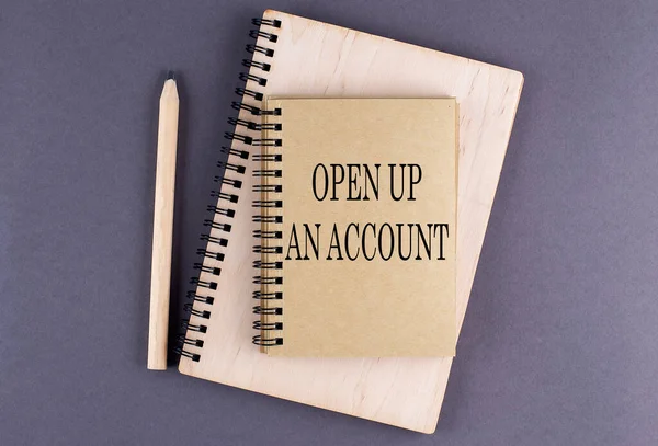 Word OPEN UP AN ACCOUNT on a notebook with pencil on the grey background