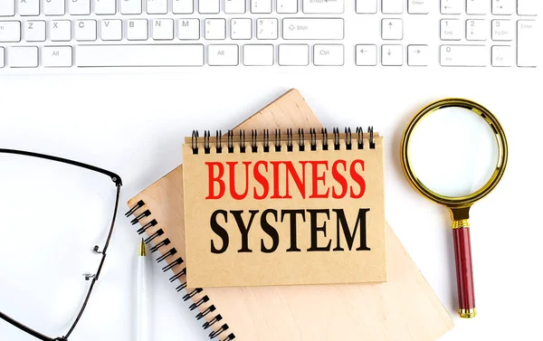 BUSINESS SYSTEM text in office notebook with keyboard, magnifier and glasses , business concept