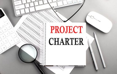 Gri arkaplan üzerinde klavye ve hesap makinesi ile not defteri üzerinde PROJECT CHARTER metni