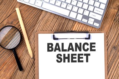 Tahta zemin üzerinde büyüteç ve klavye bulunan bir kağıt pano üzerinde balans SHEET metin