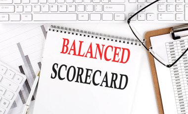 Beyaz bir arkaplan üzerinde klavye, not defteri ve analiz grafiği ile ofis masasının üzerine balanslı SCORECARD metin.