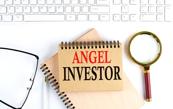 ANGEL INVESTOR text in office notebook with keyboard, magnifier and glasses , business concept