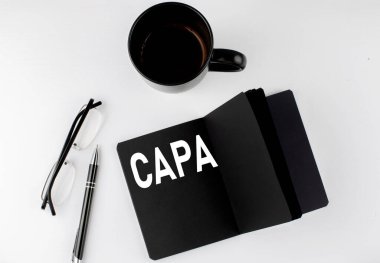 CAPA küçük siyah not defterinde beyaz arka planda kahve, kalem ve cam kaplı metinler yazdı. Siyah-beyaz stili