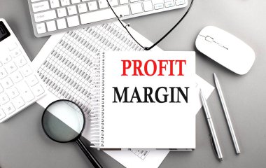 Gri arkaplan üzerinde klavye ve hesap makinesi olan bir çizelge üzerinde PROFIT MARGIN metni