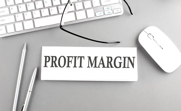 PROFIT MARGIN text on notepad on a chart with keyboard and calculator on grey background