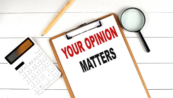 YOUR OPINION MATTERS words on clipboard, with calculator, magnifier and pencil on white wooden background