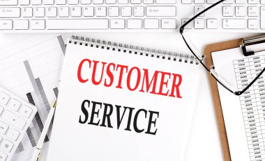 Beyaz arkaplanda klavye, not defteri ve analiz çizelgesi olan ofis masasının üzerine CUSTOMER SERVICE 'ı metin.