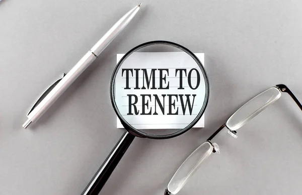 Word TIME TO RENEW on a sticky through magnifier on grey background