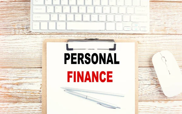 PERSONAL FINANCE text on clipboard with keyboard on wooden background