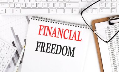 Beyaz arkaplan üzerinde klavye, not defteri ve analiz grafiği ile ofis masasında FINANCIAL FREEDOM metin.