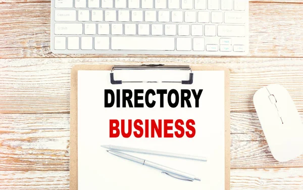 DIRECTORY BUSINESS text on clipboard with keyboard on wooden background