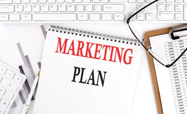 Ofis masasında beyaz bir arkaplan üzerinde klavye, not defteri ve analiz grafiği olan metin MarketiName.