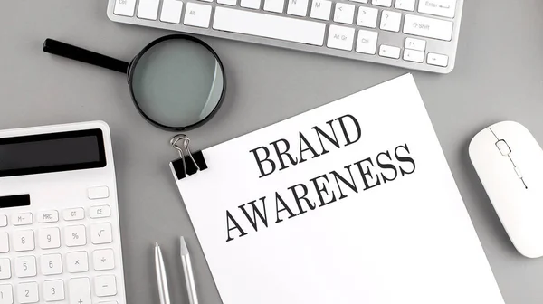 BRAND AWARENESS written on paper with office tools and keyboard on grey background