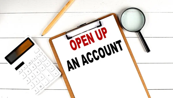 OPEN UP AN ACCOUNT words on a clipboard, with calculator, magnifier and pencil on the white wooden background