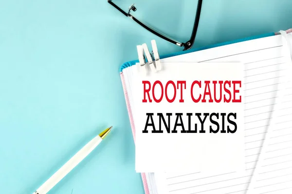 ROOT CAUSE ANALYSIS text on sticky on notebook with pen and glasses , blue background