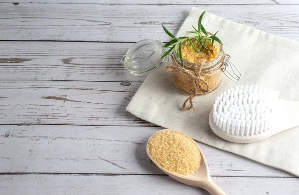 Brown sugar scrub with oil on a napkin with massage brush and sugar on spoon, wooden background, copy space