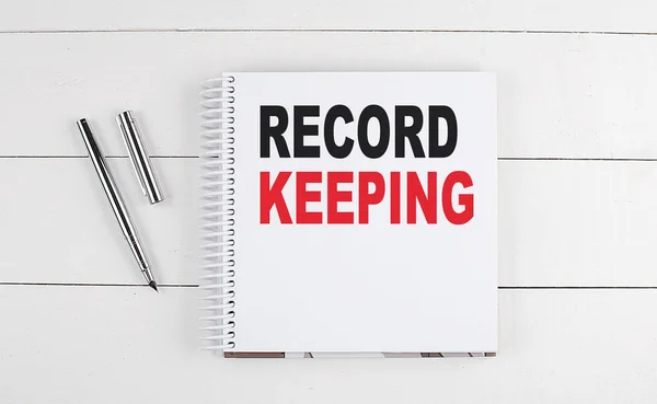 RECORD KEEPING text written on a notebook on the wooden background