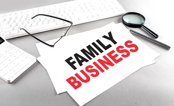 FAMILY BUSINESS text on paper on a gray background near a calculator and a white keyboard