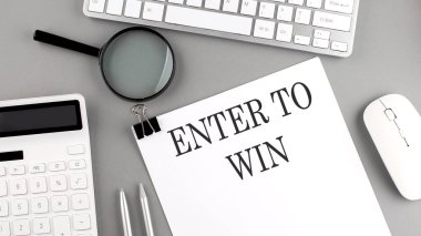 Gri arkaplan üzerinde ofis araçları ve klavye ile kağıt üzerine yazılmış ENTER To WIN