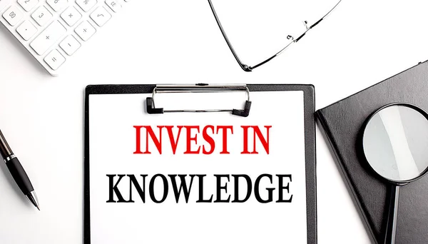 INVEST IN KNOWLEDGE text written on a paper clipboard with office tools