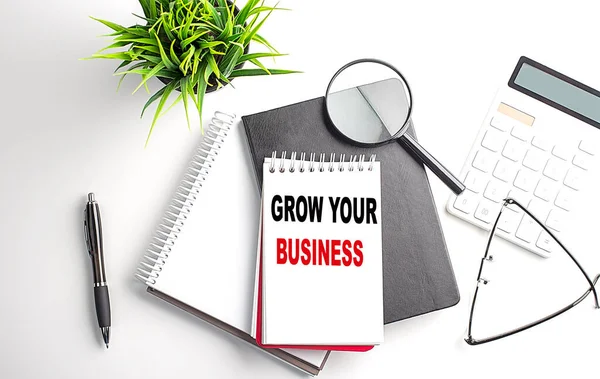 Text GROW YOUR BUSINESS on a notebook with office tools on white background