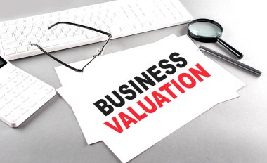 BUSINESS VALUATION text on a paper on a gray background near calculator and a white keyboard clipart