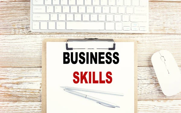 BUSINESS SKILLS text on clipboard with keyboard on wooden background