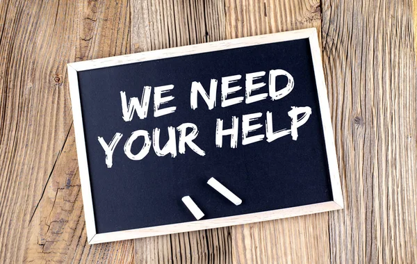 WE NEED YOUR HELP text on chalkboard on the wooden background