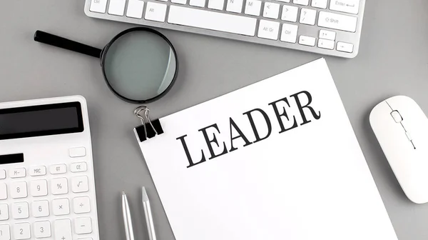LEADER written on a paper with office tools and keyboard on the grey background