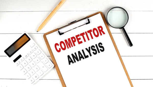 COMPETITOR ANALYSIS words on clipboard, with calculator, magnifier and pencil on white wooden background