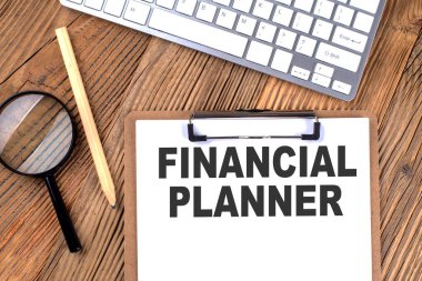 Kağıt pano üzerinde ahşap bir arka planda büyüteç ve klavye ile FINANSIAL PLANNER metin