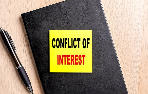 CONFLICT OF INTEREST text on sticky on black notebook with pen