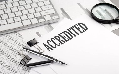 Grafikli ve klavyeli bir kağıdın üzerinde AcCREDITED metin, iş kavramı