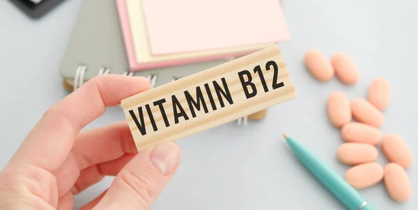 Elleri, ellerinde VITAMIN B12 yazısıyla tahta küpleri tutuyor.