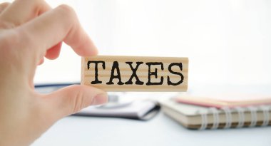 Tahta bir masadaki tahta bloklara metin vergisi. Arka planda iş kadınının elleri var. Mali konsept.