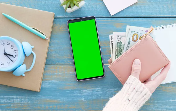 Mobile phone with green screen on a laptop and money as wooden background