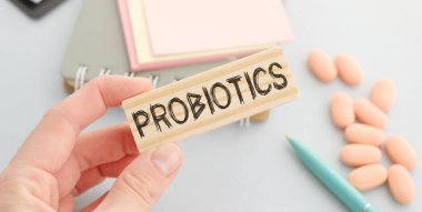PROBIOTICS kelimesi steteskopun yanındaki tahta bir bloğa yazılmış. Mavi arka planda elinde haplar ve şırınga var. Tıbbi konsept