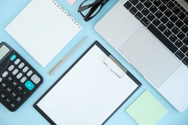 Dizüstü bilgisayarı, akıllı telefonu ve bir fincan kahveli diğer iş malzemeleri olan mavi masa ofisi. Metni kopyalamak için üst görünümü kullan. Desenci çalışma alanı düz masa üzerinde temel elementler yatıyordu.