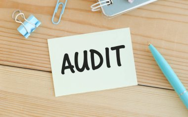 AUDIT yazılı beyaz bir kart, kitapların arka planına karşı masada duran kağıtlar için bir şarjör üzerinde duruyor. Odaklanmayın