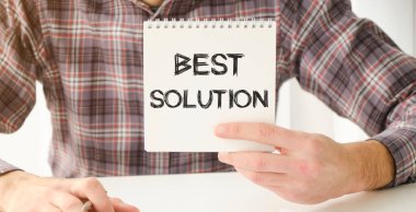 Ofis masasında BEST SOLUTION metni olan defter, belgeler, hesap makinesi, gözlük ve kalem.