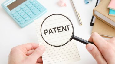 Kağıt not defteri, metin PATENT, buruşmuş kağıtlar ve koyu arkaplanda büyüteç